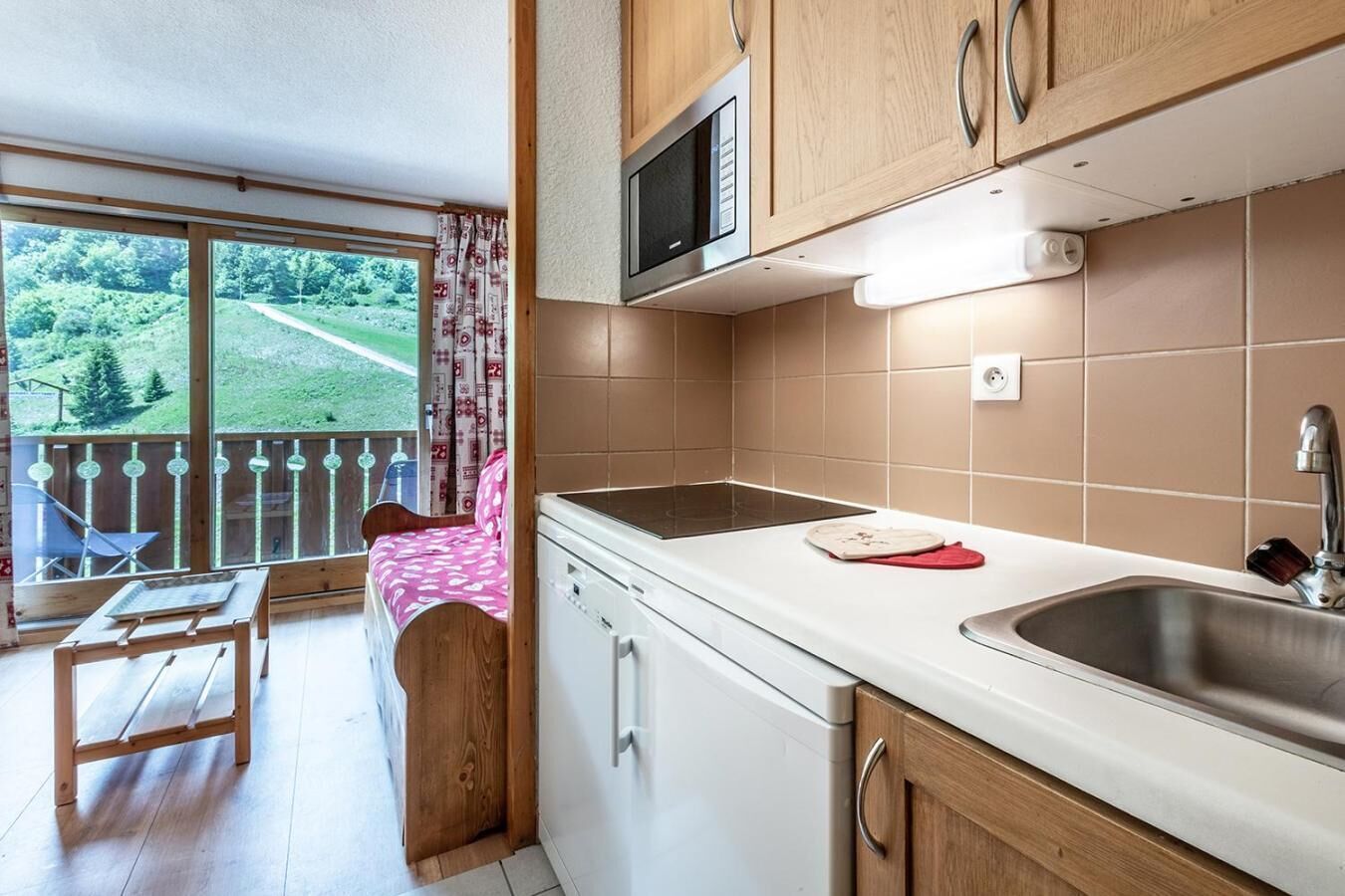 Una cucina con forno a microonde, lavello e mobili in legno. È presente un balcone con vista su spazi verdi.