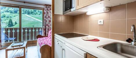 Una cucina con forno a microonde, lavello e mobili in legno. È presente un balcone con vista su spazi verdi.