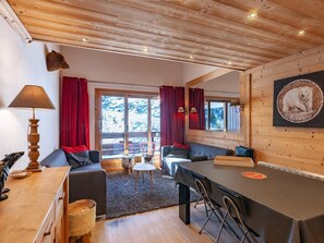 Interior acogedor de una cabaña con techo de madera, un sofá, una mesa de comedor y un ventanal con cortinas rojas.