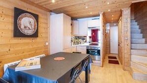 A modern kitchen with wooden cabinets, a dining table with chairs, and a staircase leading to another level.
