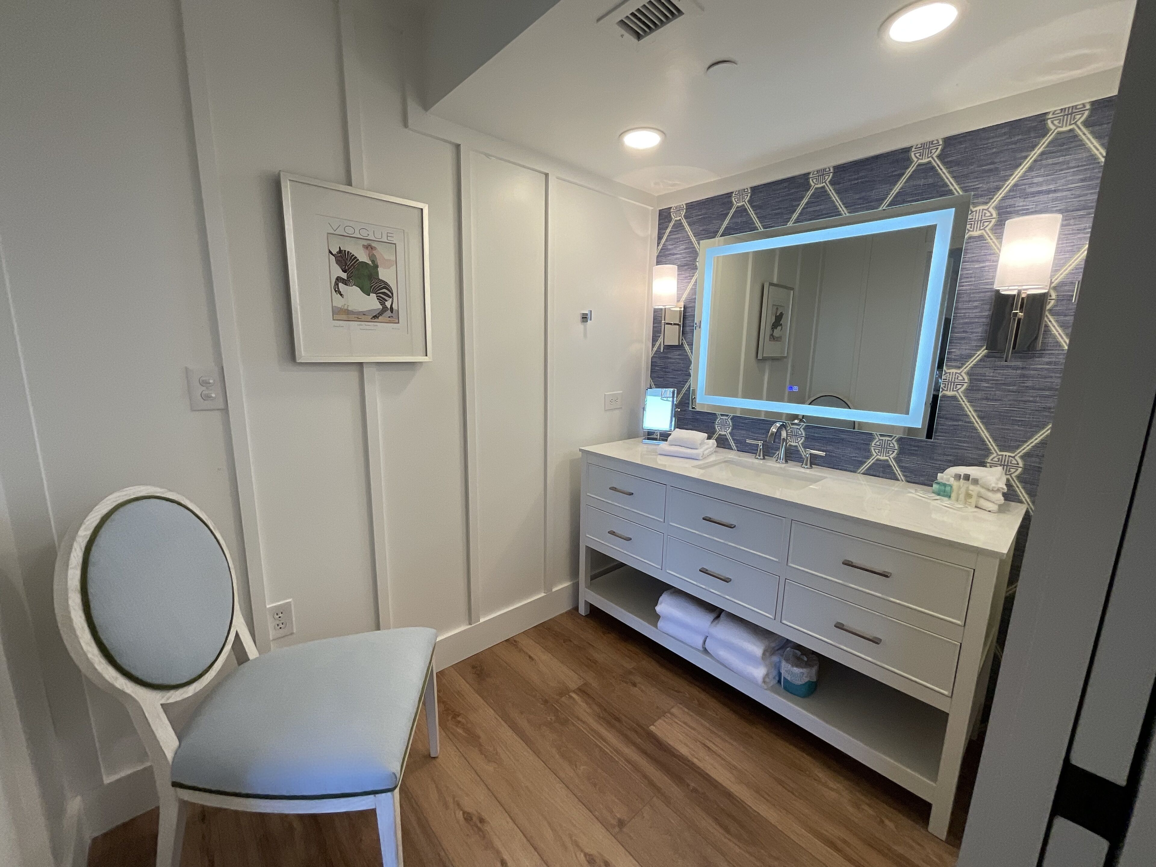 A modern bathroom with a white vanity, a large mirror, and a framed picture on the wall.