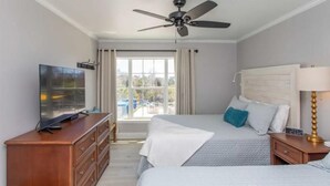 Ein Hotelzimmer mit einem Bett, einem Fernseher auf einer Holzkommode, einem Deckenventilator und einem Fenster mit Vorhängen.