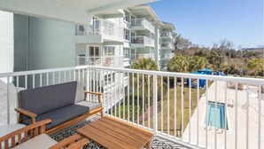 Ein Balkon mit einer Couch, einem Holztisch und Stühlen mit Blick auf einen Swimmingpool und einen Spielplatz.