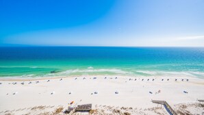 Ein Strand mit blauem Himmel, sandigem Ufer und einer Holzpromenade, die zum Wasser führt.