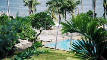 A pool area with palm trees, lounge chairs, and a view of the ocean.