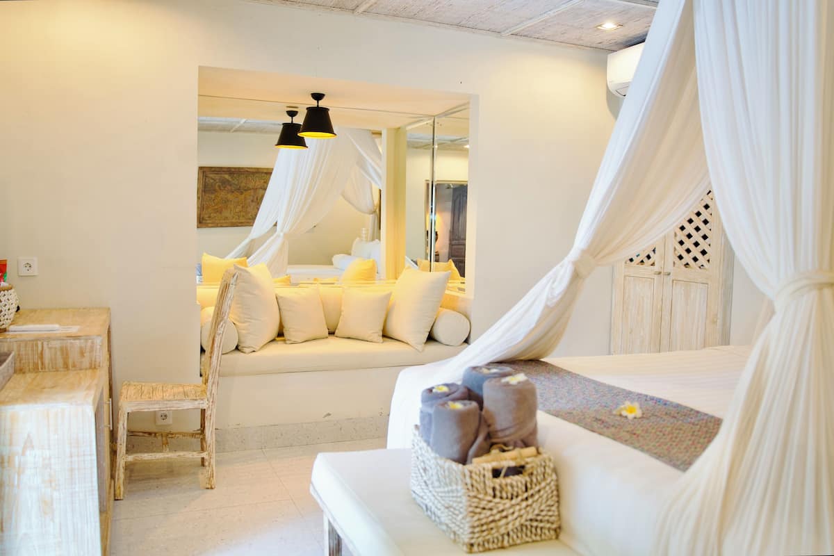 A bedroom with a bed, a bench, and a chair. There is a basket with towels on the bed.