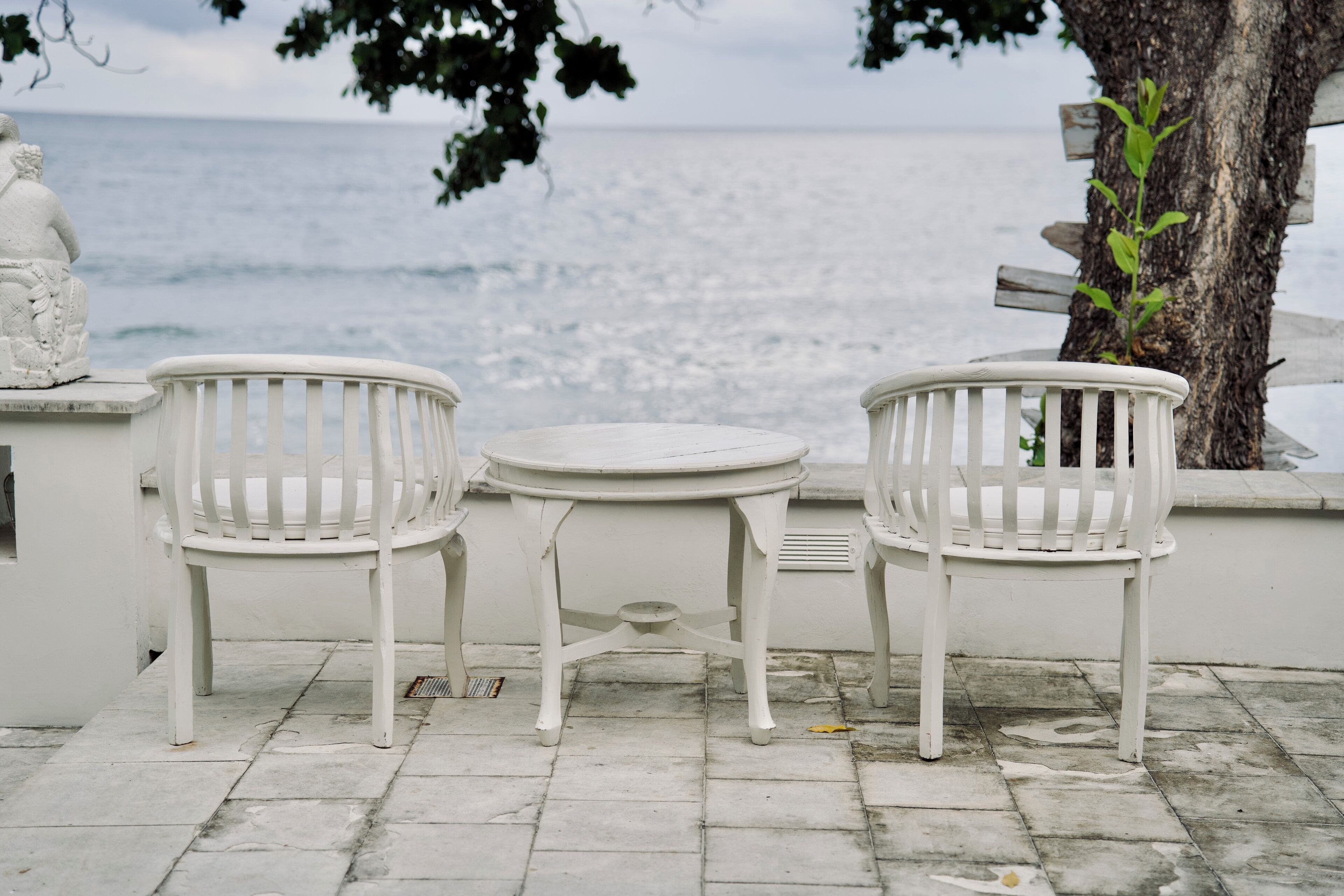 Un espace extérieur aménagé avec des sièges blancs, comprenant deux chaises et une petite table, offrant une vue sur la mer.