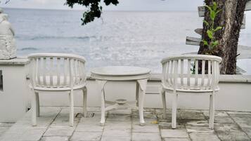 Un espace extérieur aménagé avec des sièges blancs, comprenant deux chaises et une petite table, offrant une vue sur la mer.