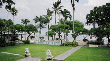 A poolside area with palm trees, a stone pathway, and two stone statues.