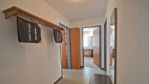Un couloir avec un banc en bois, un porte-manteau orné d’une pancarte indiquant « Vacances zéro déchet », et un miroir sur le mur de droite.