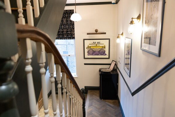 A staircase with white balusters, a black wall with framed artwork, and a hanging light fixture. - THE KNIGHT OF NOTTINGHILL (London)