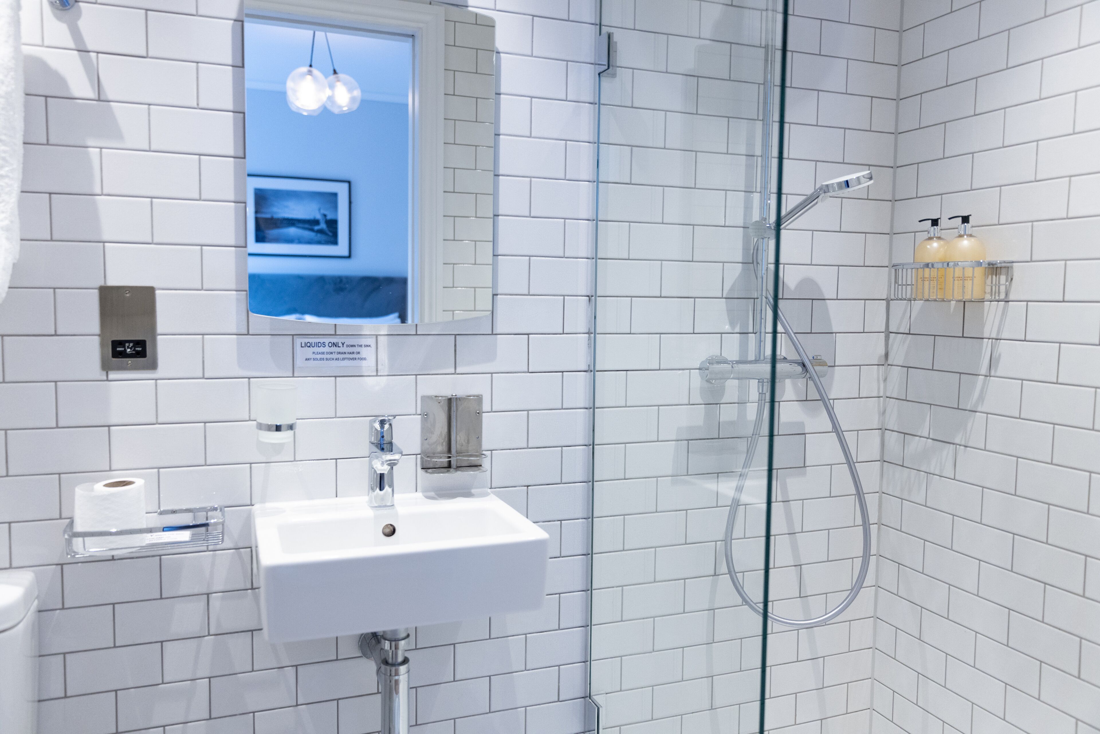 Un bagno moderno con piastrelle bianche, una doccia vetrata, un lavandino e uno specchio con cornice.