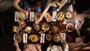 A group of people dining at a wooden table with various dishes. - THE KNIGHT OF NOTTINGHILL (London)