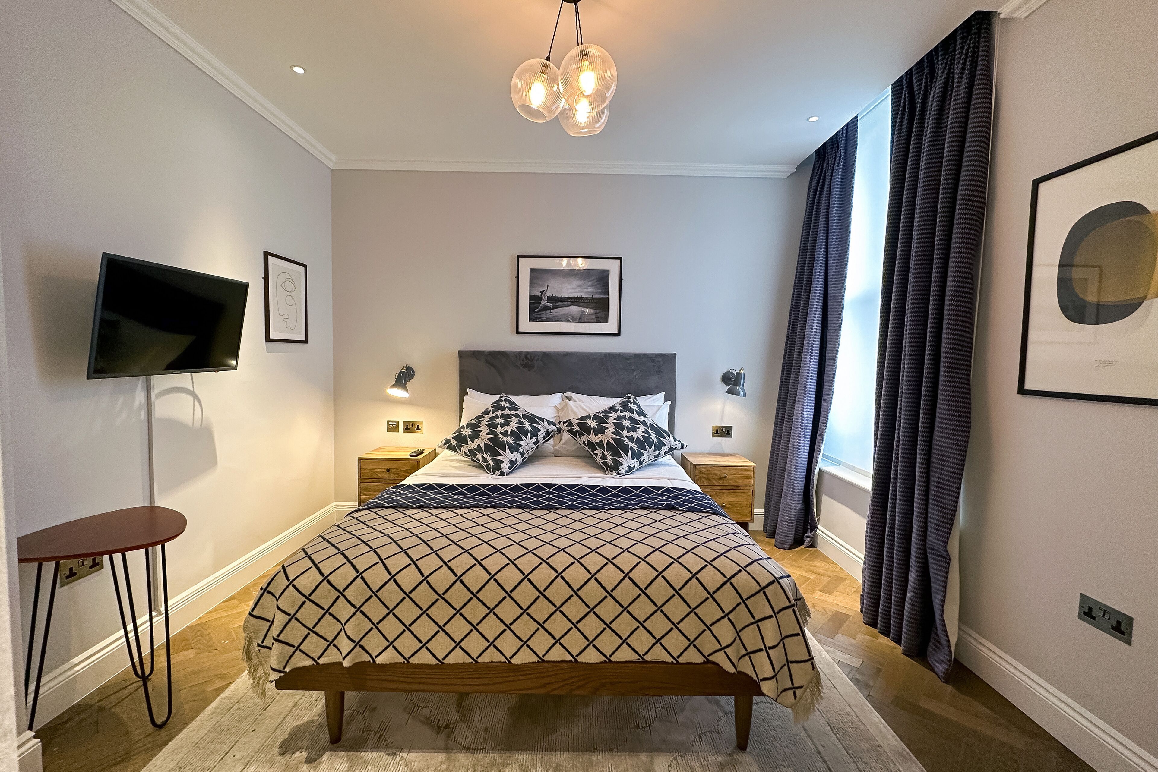 A bedroom with a bed, bedside tables, a TV, and a ceiling light fixture.
