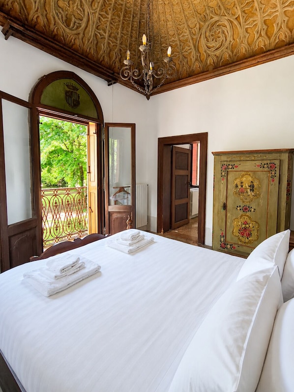 Une chambre d’hôtel avec un grand lit, un lustre, un plafond en bois et une vue sur la verdure.