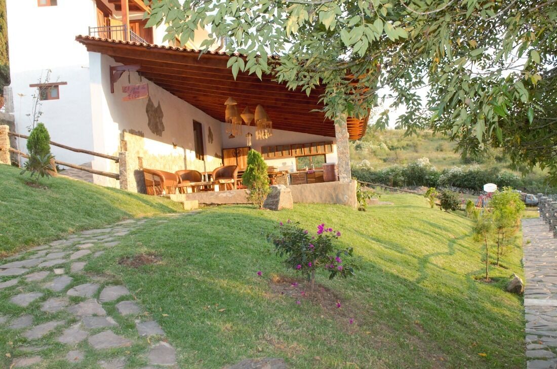 A rustic building with a covered patio, stone pathway, and a small garden with flowers and shrubs.