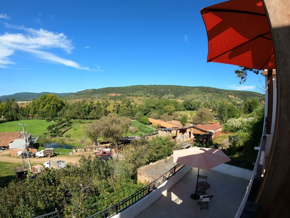 A balcony with a red umbrella, overlooking a green valley with houses and trees. - La Toscanía Tapalpa Resort & Agroturismo (Tapalpa)