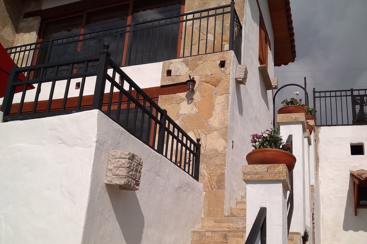 Un edificio blanco con fachada de piedra, barandilla de metal negro y una escalera que lleva a un balcón con toldo rojo.
