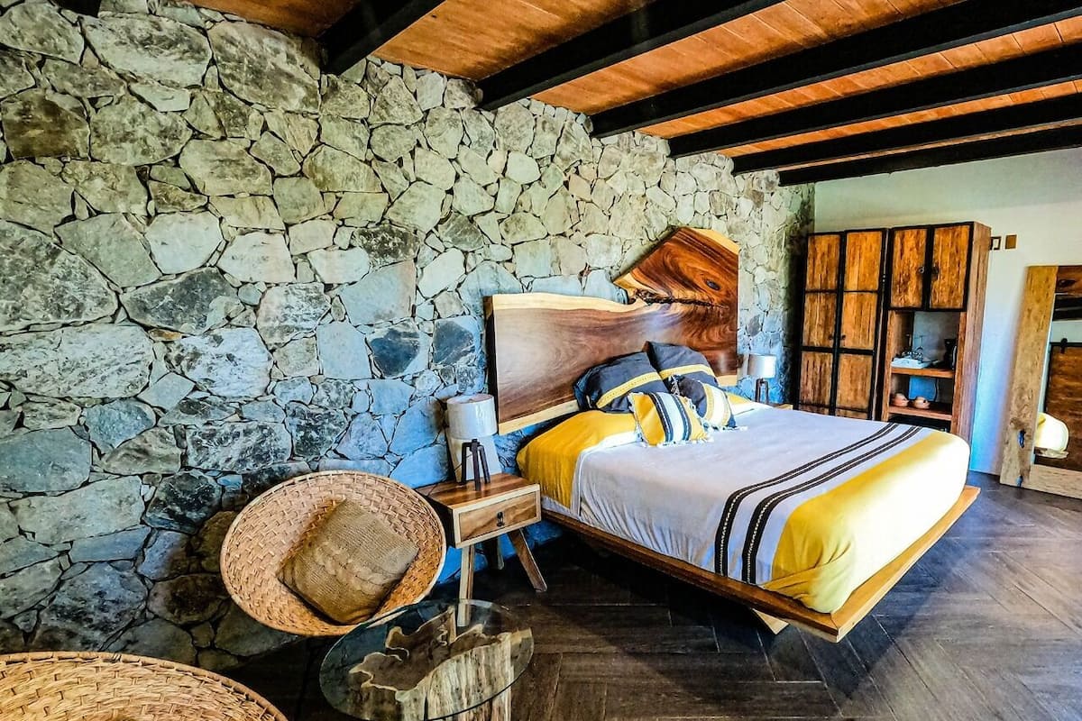 Un dormitorio con pared de piedra, estructura de cama de madera y suelo con patrón de espiga.