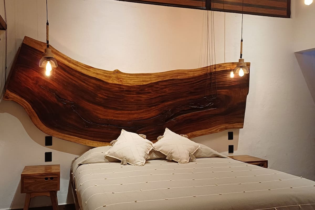 Un dormitorio con una cabecera de madera original, una cama con colcha a rayas y dos mesitas de noche.