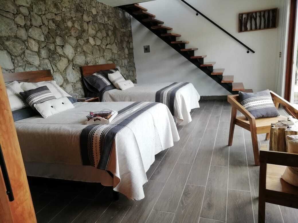 Un dormitorio con dos camas, una pared de piedra, una escalera de madera y vistas al exterior.