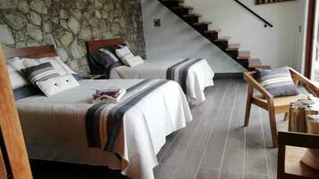 Un dormitorio con dos camas, una pared de piedra, una escalera de madera y vistas al exterior.