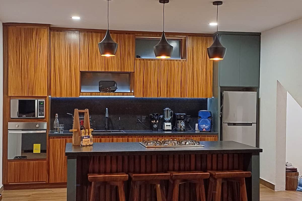 Una cocina moderna con armarios de madera, una isla central con taburetes, un microondas y un refrigerador.