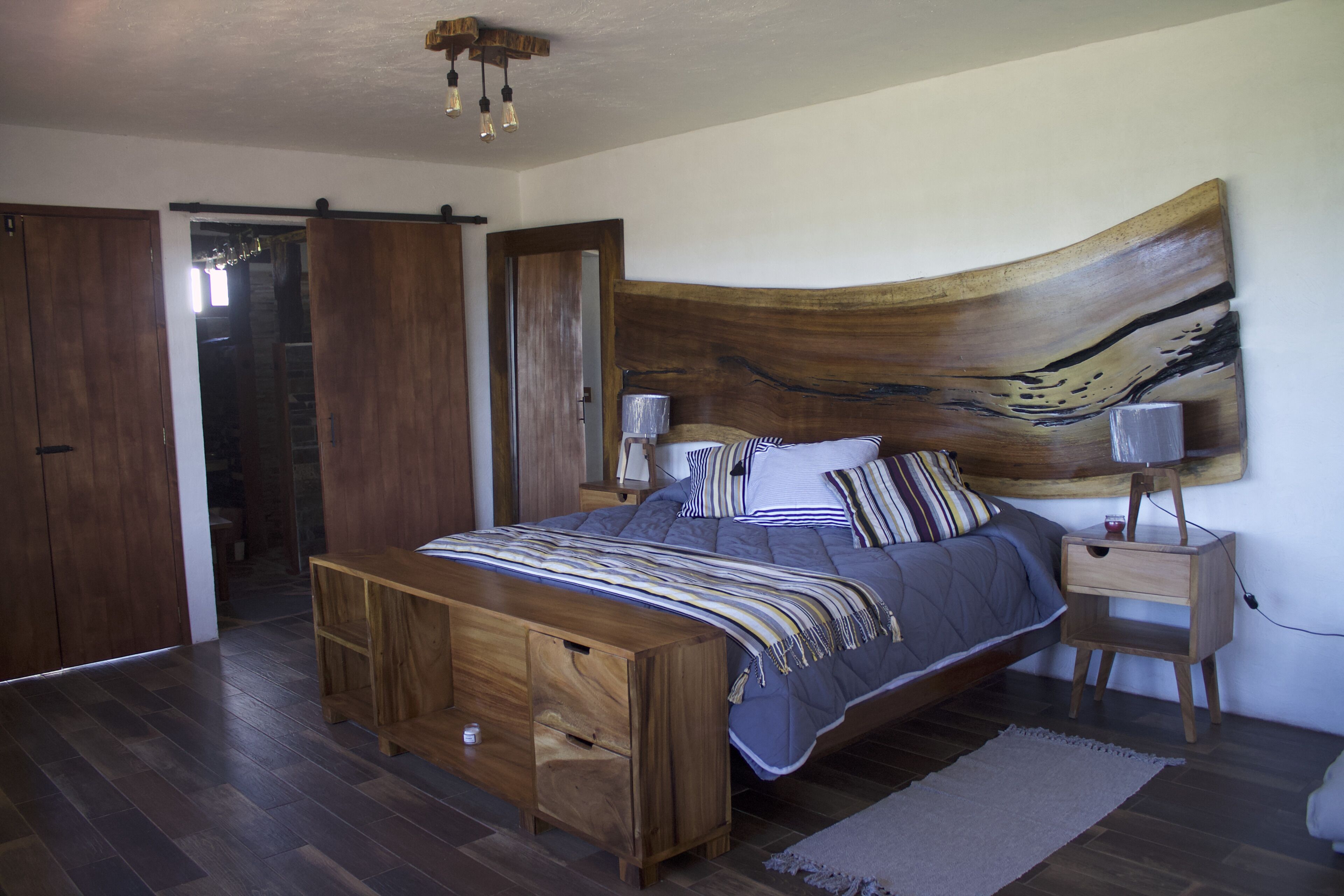Un dormitorio con cama de madera, mesita de noche, lámpara de pared y un cuadro abstracto grande.