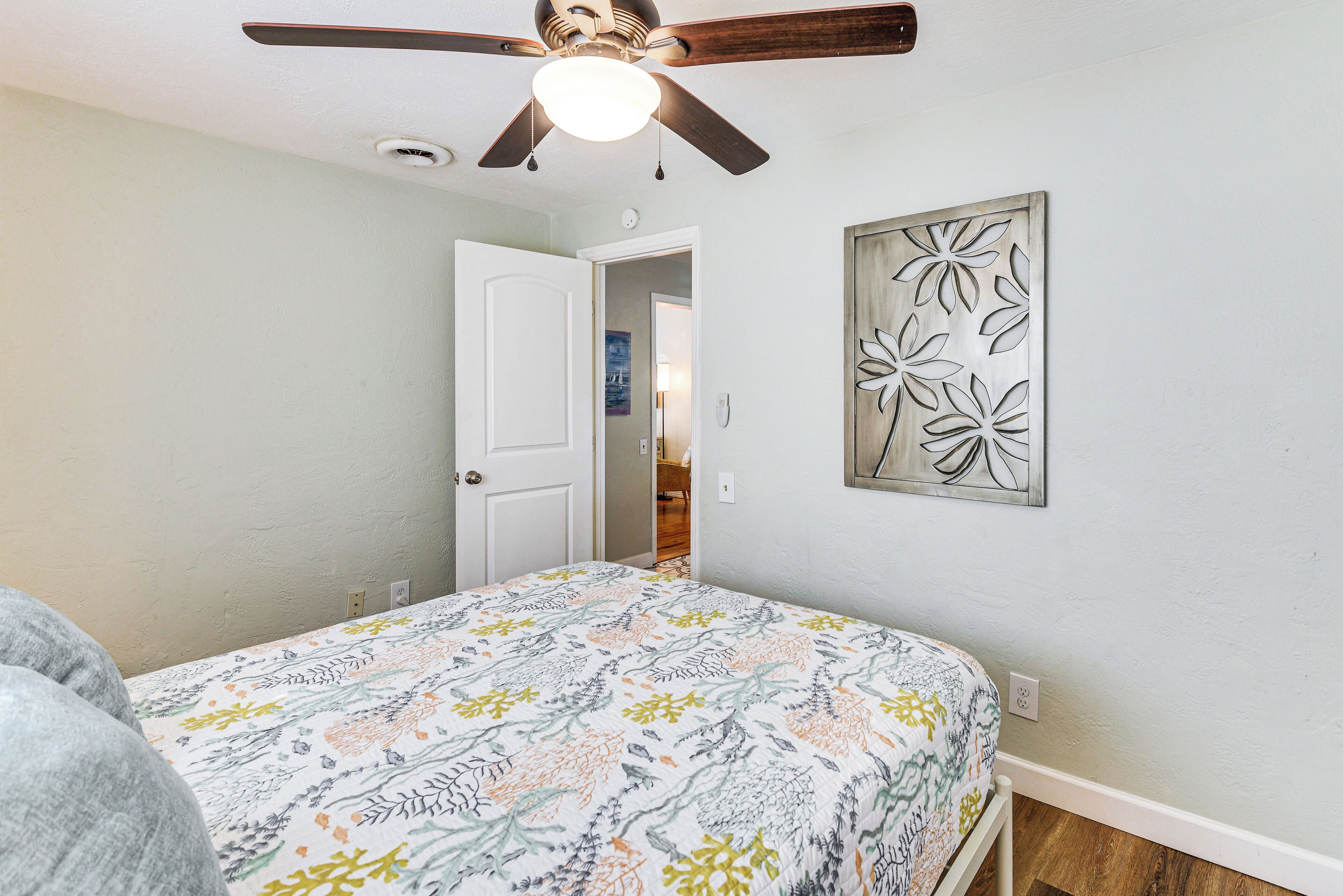 A bedroom with a bed, a ceiling fan, a door, and a wall-mounted artwork.