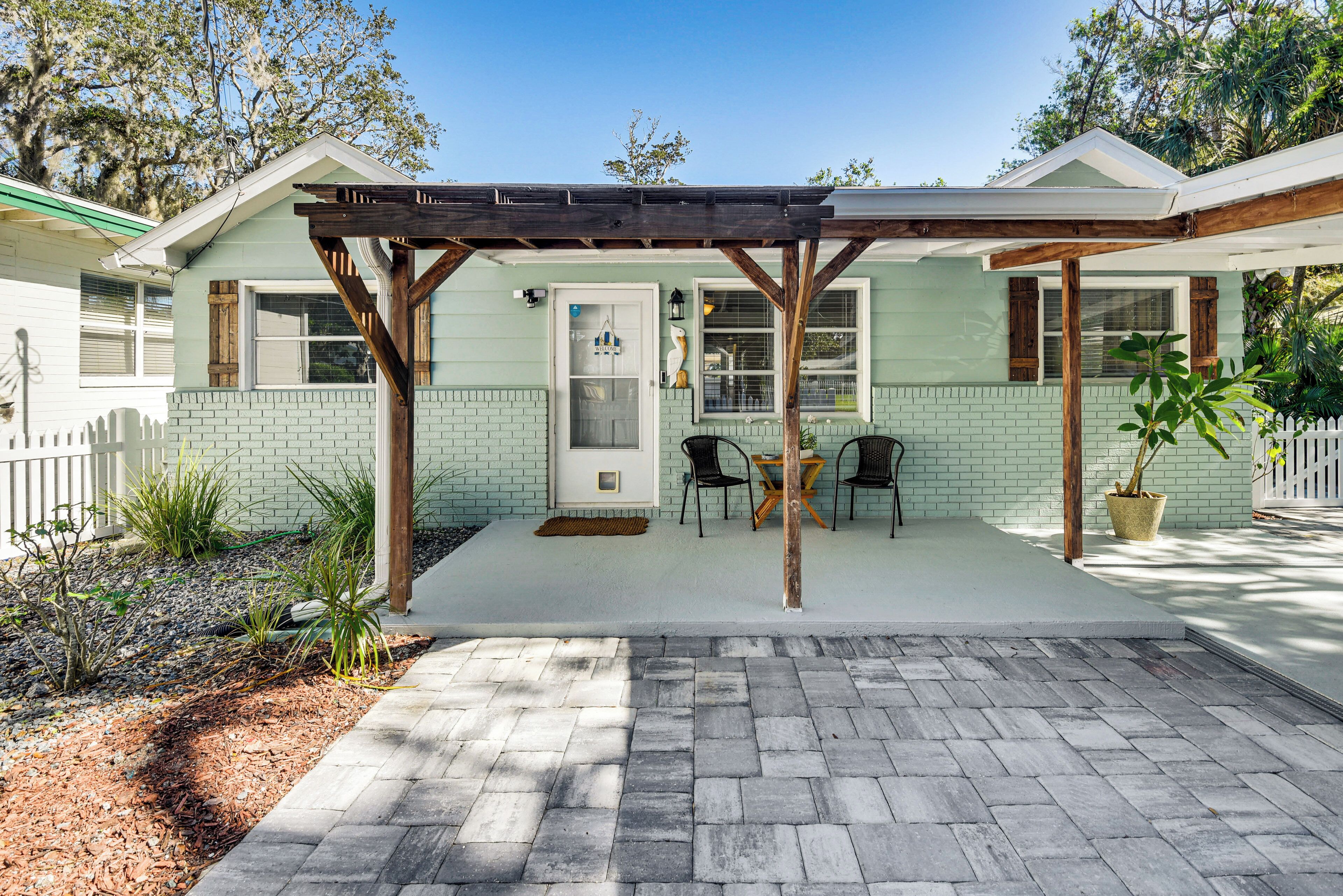 A covered patio with a brick floor, a wooden pergola, and a small table with chairs.