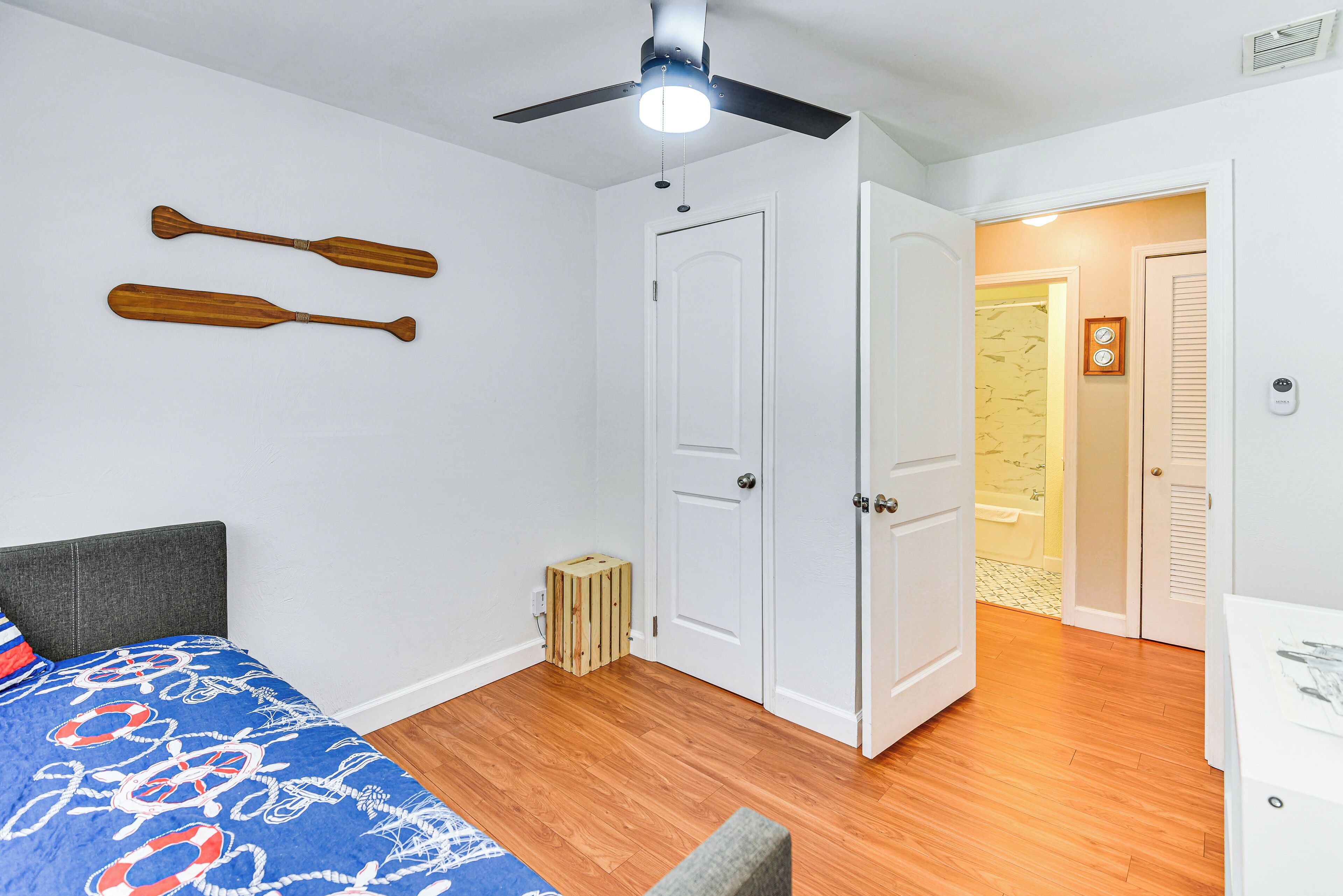 A bedroom with a bed, a ceiling fan, a door, and a small wooden stool.