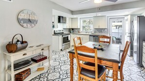 Una cocina moderna con armarios blancos, una mesa de comedor con sillas, un reloj en la pared y un ventilador de techo.