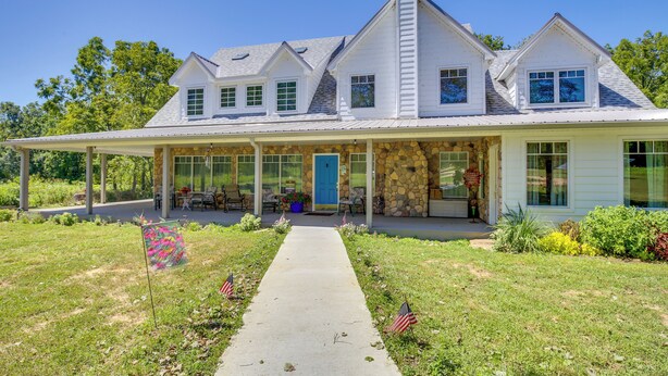 A two-story house with a covered porch, stone facade, and a blue door. - Spacious & Secluded Shook Home w/ Private Hot Tub! (Lowndes)