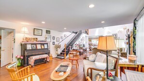 A spacious living room with a piano, wooden chairs, a sofa, and a staircase leading to an upper floor. - Spacious & Secluded Shook Home w/ Private Hot Tub! (Lowndes)