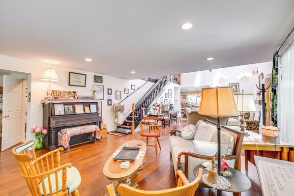 A spacious living room with a piano, wooden chairs, a sofa, and a staircase leading to an upper floor. - Spacious & Secluded Shook Home w/ Private Hot Tub! (Lowndes)