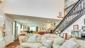 A spacious living room with a large sectional sofa, a staircase with a wrought iron railing, and a dining area in the background. - Spacious & Secluded Shook Home w/ Private Hot Tub! (Lowndes)