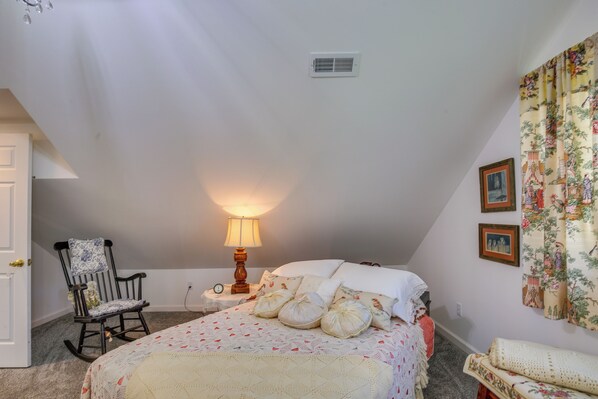 A cozy bedroom with a bed, a rocking chair, a lamp, and a floral curtain. - Spacious & Secluded Shook Home w/ Private Hot Tub! (Lowndes)