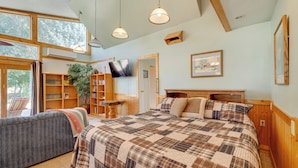 A cozy bedroom with a large bed, a sofa, and a TV. There are wooden shelves and a plant. - Cozy Idaho Retreat w/ Grill & Fire Pit! (Caldwell)