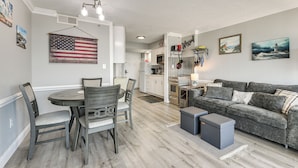 A dining area with a table and chairs, a gray sofa, and a kitchen in the background. - Pool Access: 8th-floor Condo on North Myrtle Beach (North Myrtle Beach)