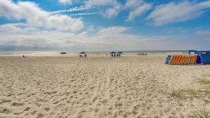 A sandy beach with umbrellas and beach chairs, a lifeguard tower, and the ocean in the background. - Pool Access: 8th-floor Condo on North Myrtle Beach (North Myrtle Beach)