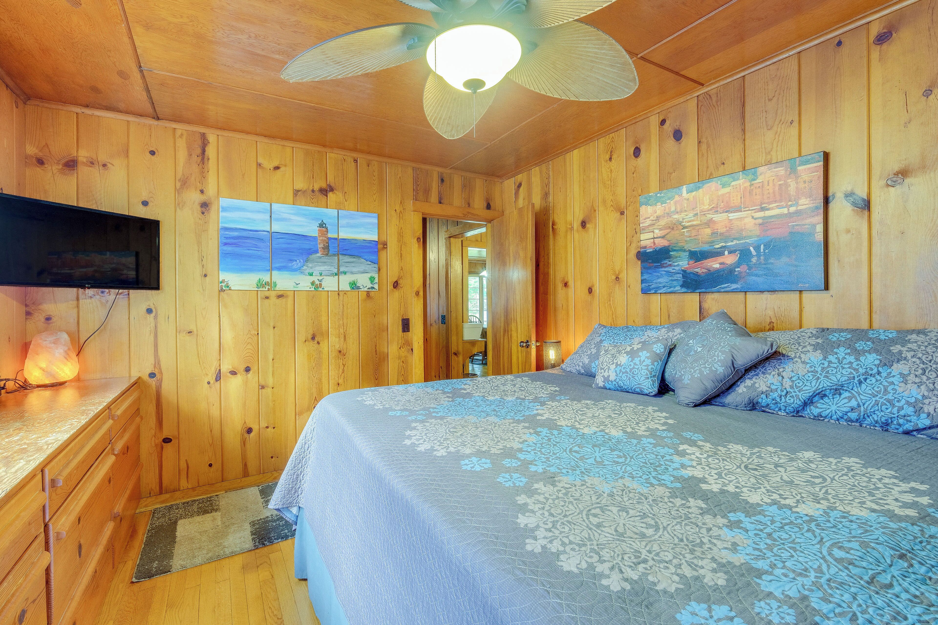 Une chambre dans une cabane en bois, avec un lit, un ventilateur de plafond, un tableau et un téléviseur.