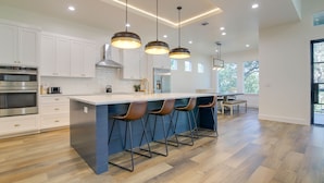A modern kitchen with white cabinets, a central island with bar stools, stainless steel appliances, and pendant lighting. - Modern Kingsland Home w/ River Access & Kayaks! (Kingsland)