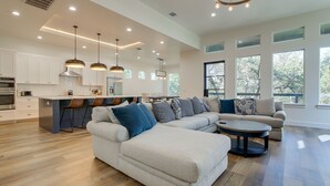 A spacious living room with a large L-shaped sofa, a coffee table, and a kitchen area with white cabinets and a central island. - Modern Kingsland Home w/ River Access & Kayaks! (Kingsland)