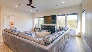 A modern living room with a large sectional sofa, a flat-screen TV, and a ceiling fan. - Modern Kingsland Home w/ River Access & Kayaks! (Kingsland)