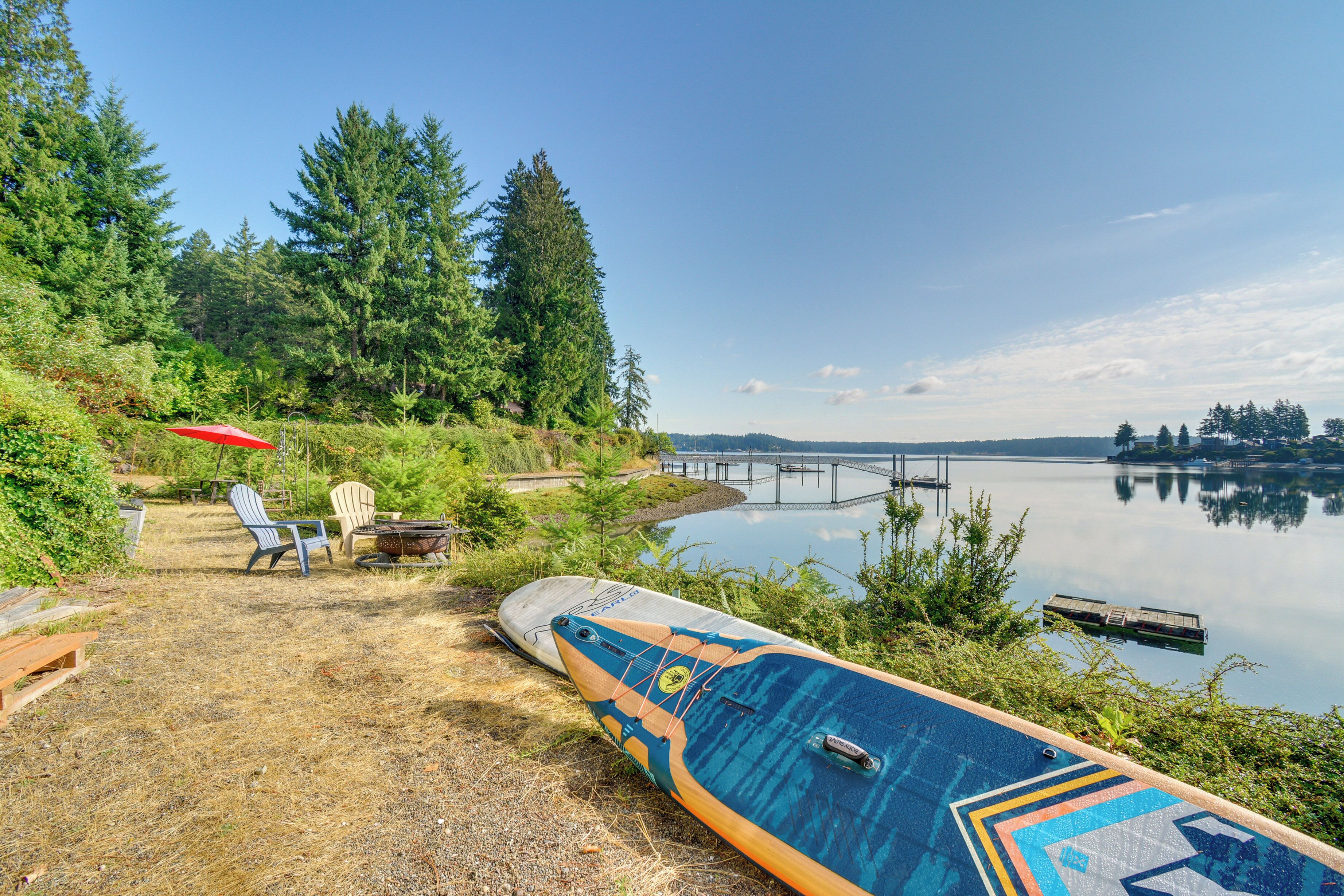 A lakeside setting with a paddleboard, chairs, and a red umbrella.