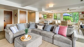 A spacious living room with a large grey sectional sofa, a coffee table with decorative items, and a view of the kitchen and dining area through large windows. - Waterfront Allyn Retreat w/ Guest House & Beach! (Allyn)