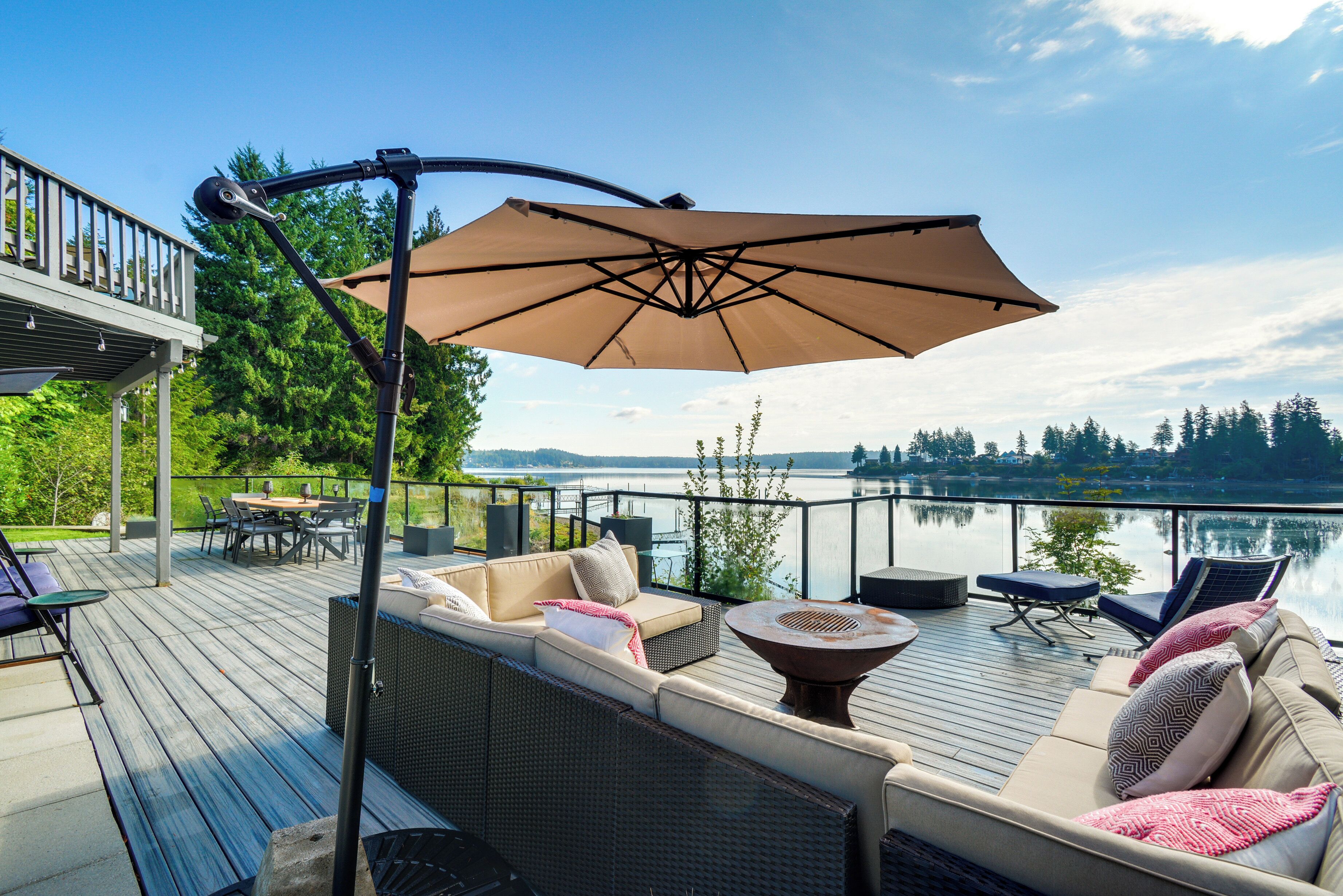 Um deck com móveis de exterior, um guarda-sol grande e vista para um lago.