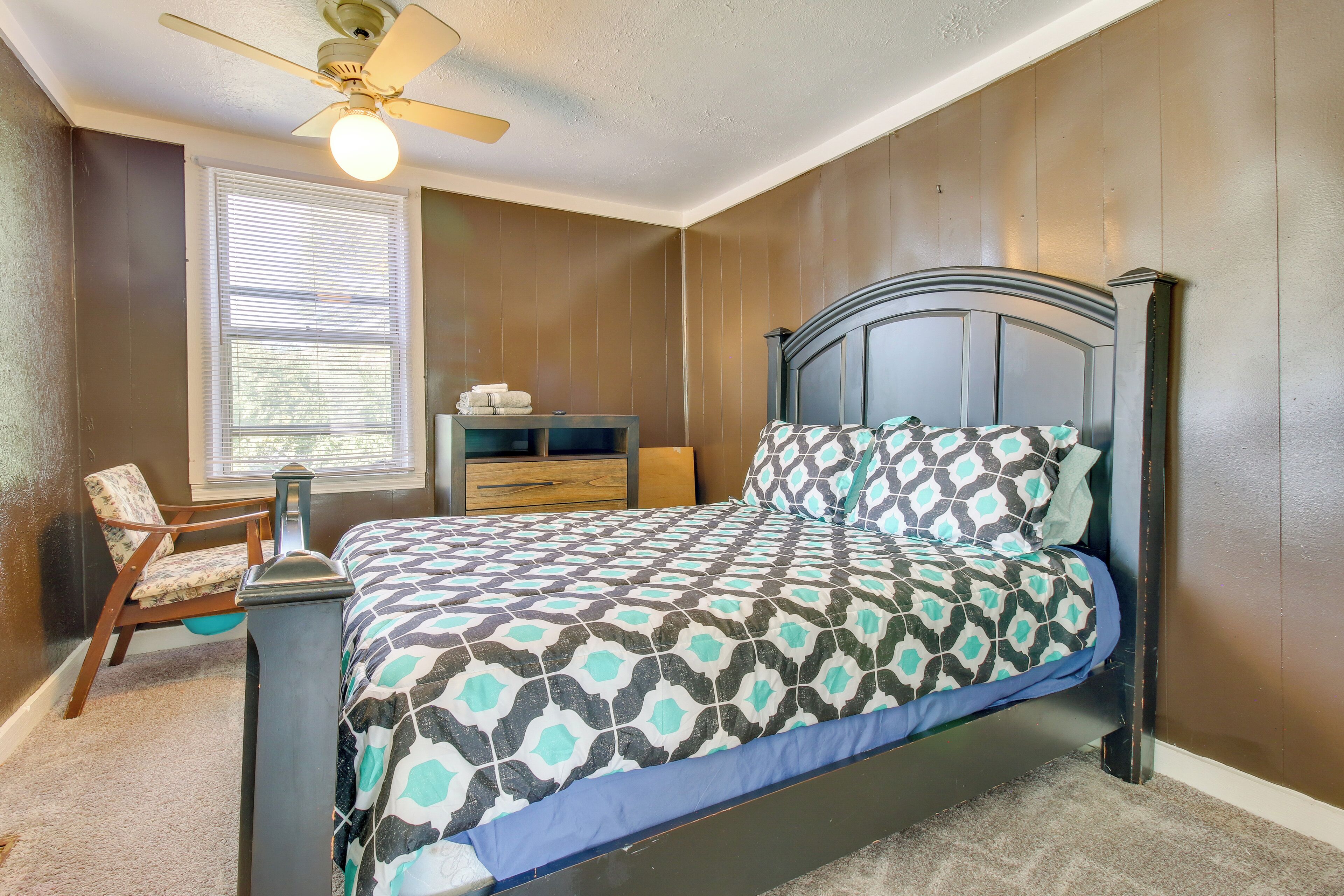 A bedroom with a bed, a chair, a nightstand, a window with blinds, and a ceiling fan.
