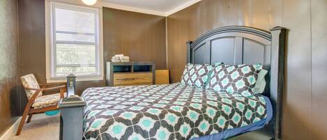 A bedroom with a bed, a chair, a nightstand, a window with blinds, and a ceiling fan.