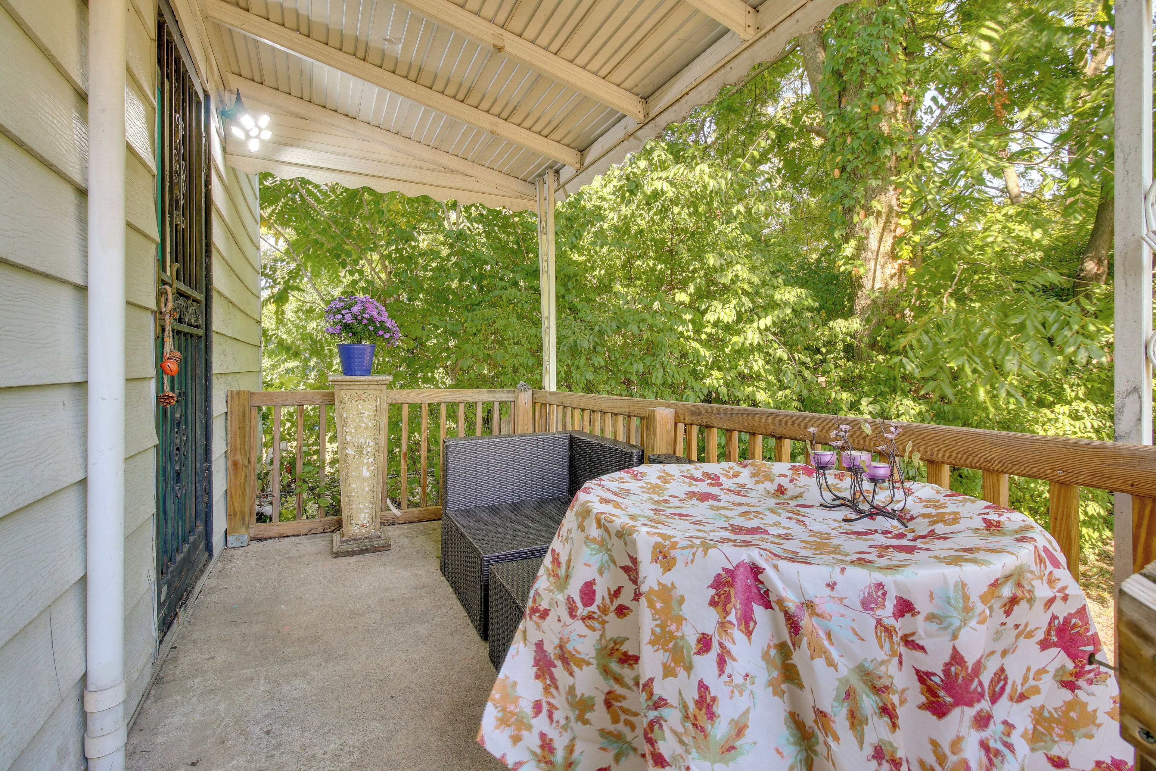 Une véranda abritée, avec une table et des chaises, entourée de verdure.